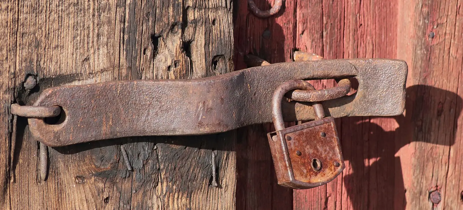 Cadeado enferrujado pendurado em uma tranca de uma porta de madeira