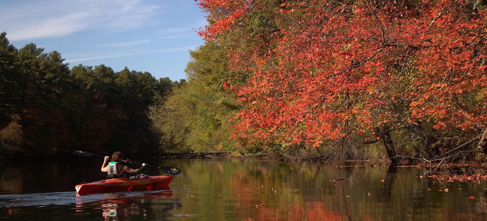Red kayak on a calm river lined with autumn-leaved trees